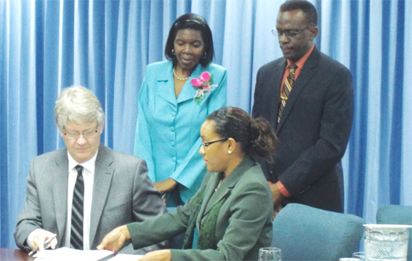 Tom Mercer (left) of Stantec and Dr. Alison Gajadhar Permanent Secretary in the Ministry of Infrastructure, Port services and Transport affixing their signatures to the agreement. Looking on are Phillip J. Pierre, Infrastructure Minister and Emma Hippolyte, Commerce Minister.