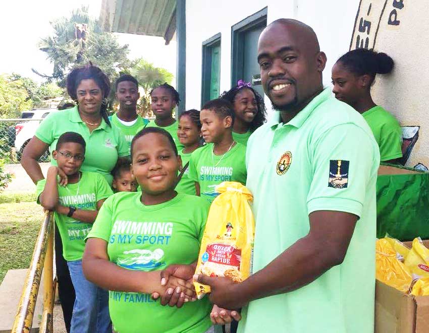 Image: A young male swimmer from LASC presenting a food item to school principal, Ezra Joseph. (Photo: LASC)