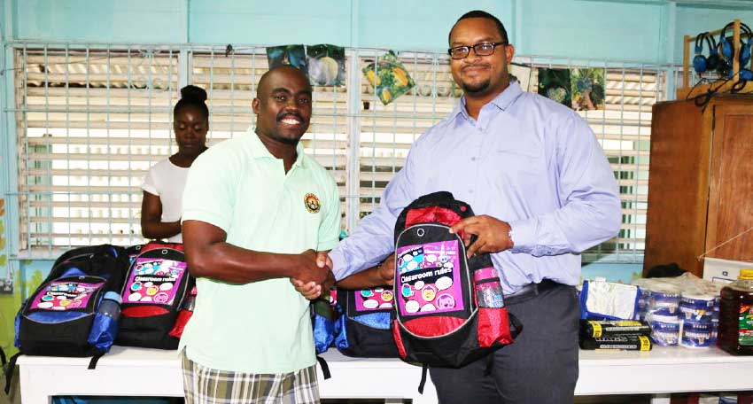 Image: OECS’ Daniel Campbell (left) hands supplies to Mr Erza Joseph, Principal of the Des Barras School (at right).