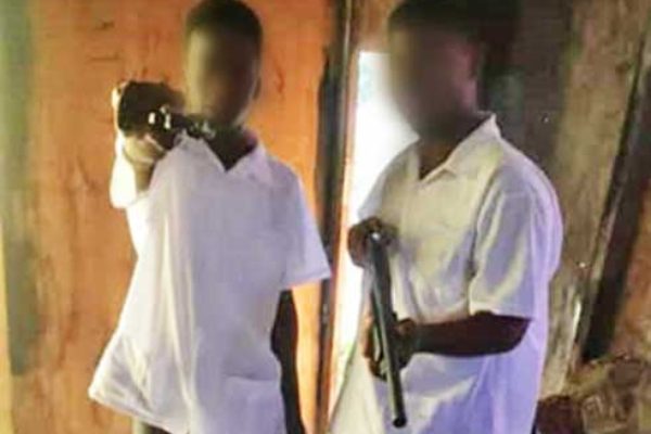 Image: Two boys pictured in full secondary school uniform with what appears to be firearms (a hand gun and shot gun).