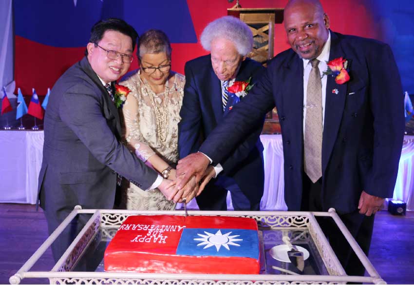 Image: The joining of hands during the cake cutting. From left: Charge d’Affaires at the Embassy of Taiwan Bill Shih-Chang Huang, Lady Cenac, Governor General Sir Neville Cenac and Minister Ezechiel Joseph. 