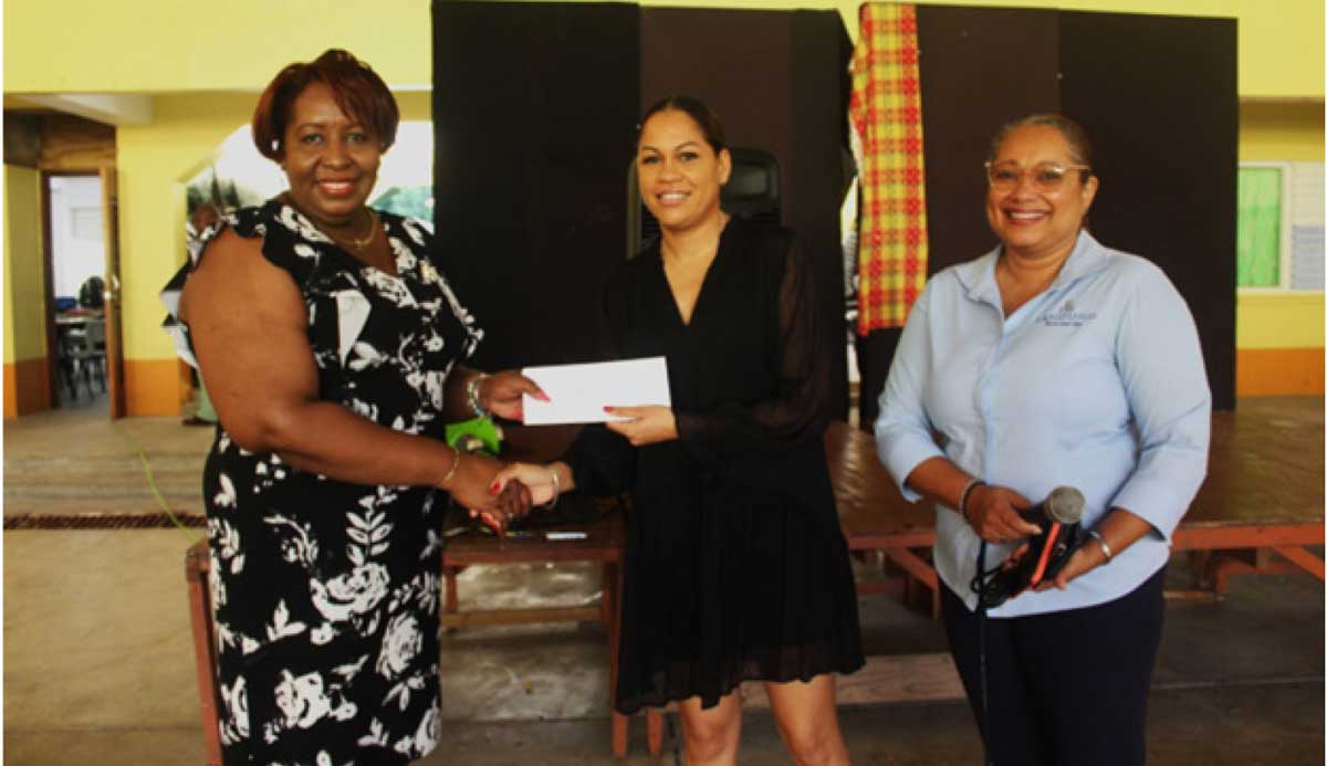 Ethelene Leonce, Principal of Dame Pearlette Louisy Primary School, receives the cheque from Shellone Surage, Legal and Compliance Officer at The Landings, at the school assembly. At far right is Kamille Huggins, Residences Manager at The Landings.