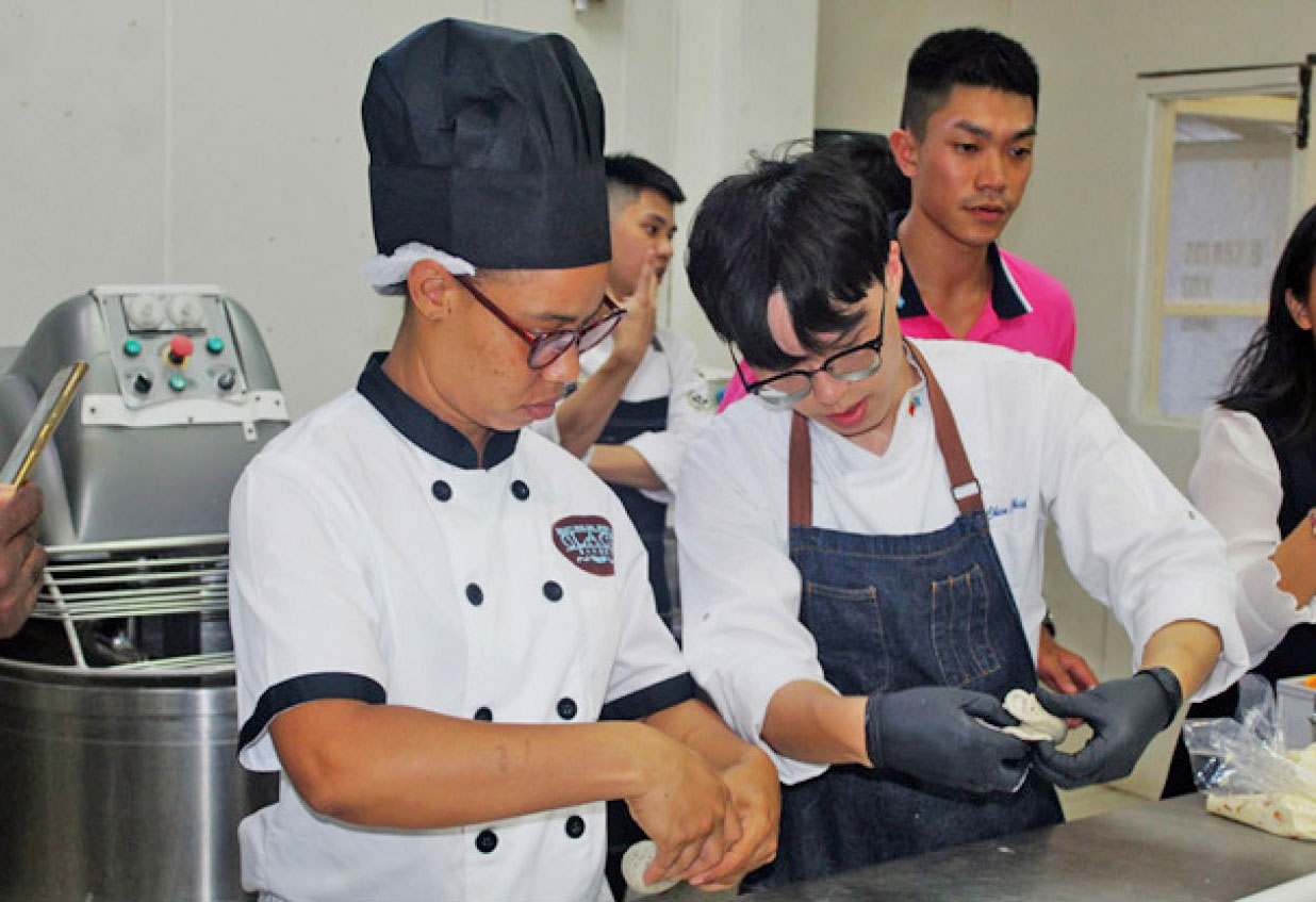 Chef Louis Hsieh, a Taiwan Youth Ambassador, right, demonstrates to a local baker how to fold a bagel during the bakery workshop at Glace Bakery on Wednesday, September 6.